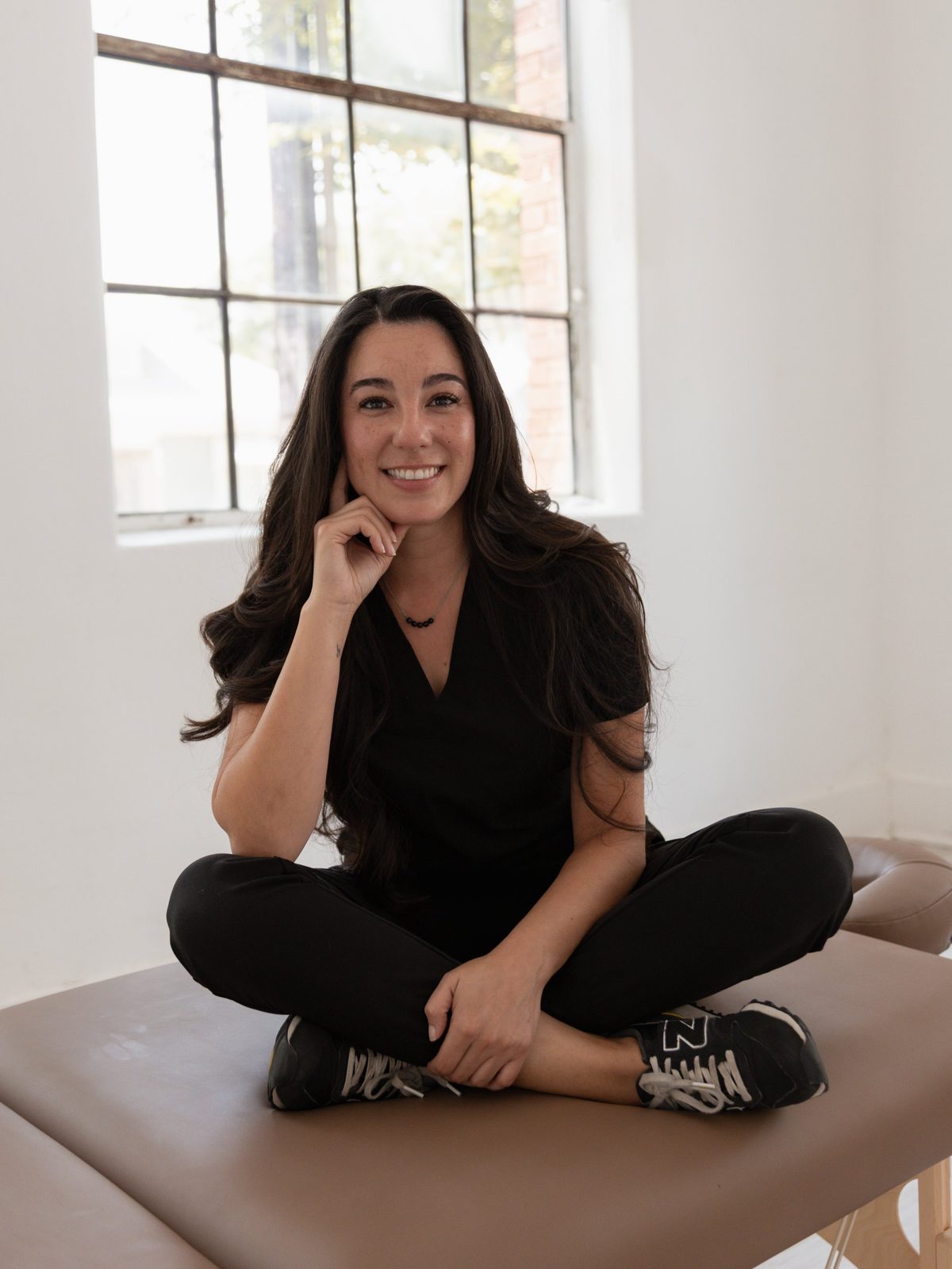 Valerie Vazquez, massage therapist, seated cross-legged on her table in a bright studio in downtown Fort Worth
